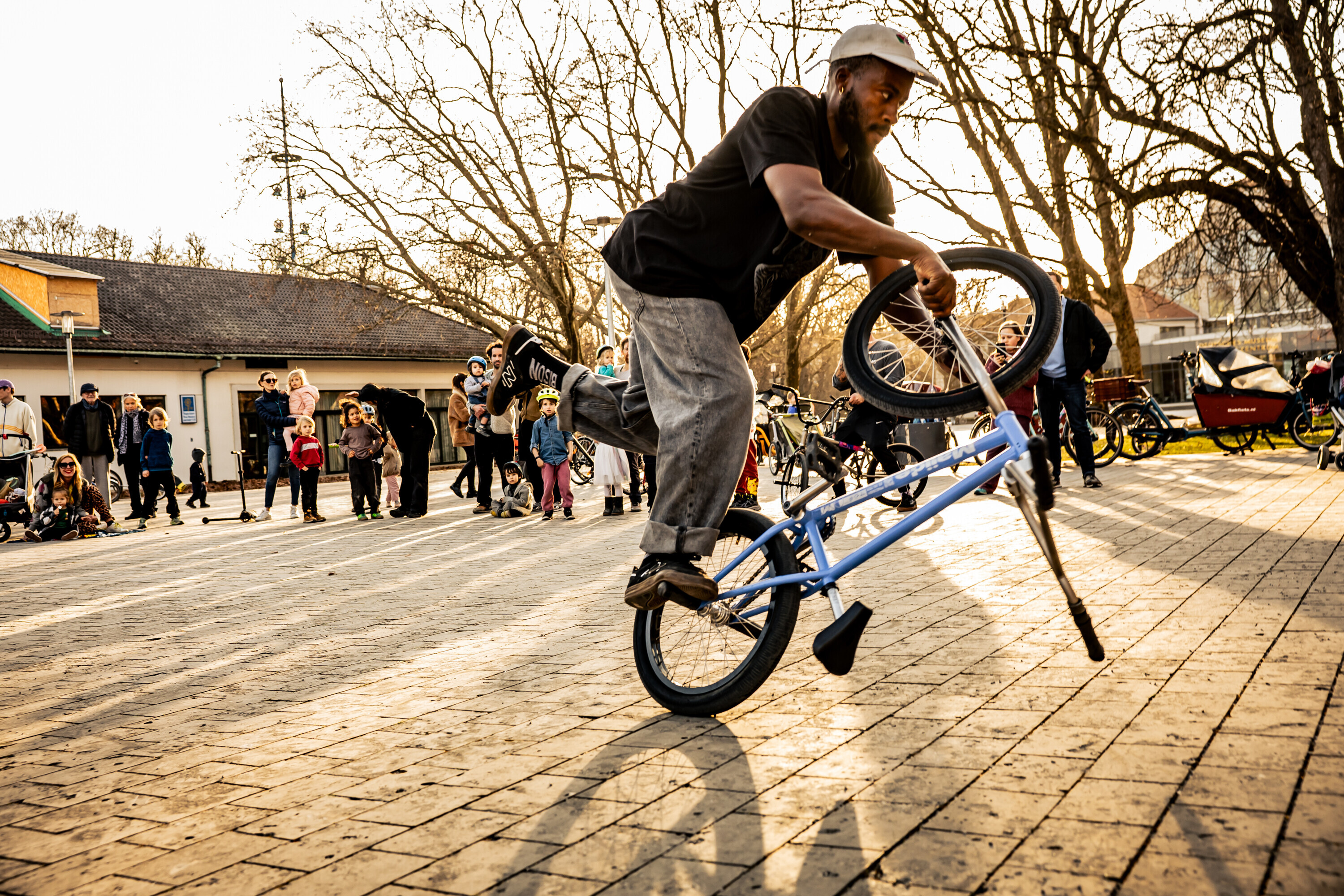 Omari Cato performing a flatland BMX trick on a city square with people watching.